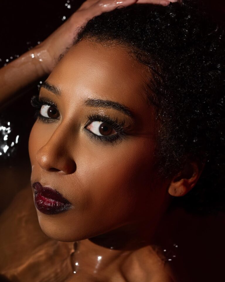 Black model with grungy makeup posing under water for beauty photoshoot.